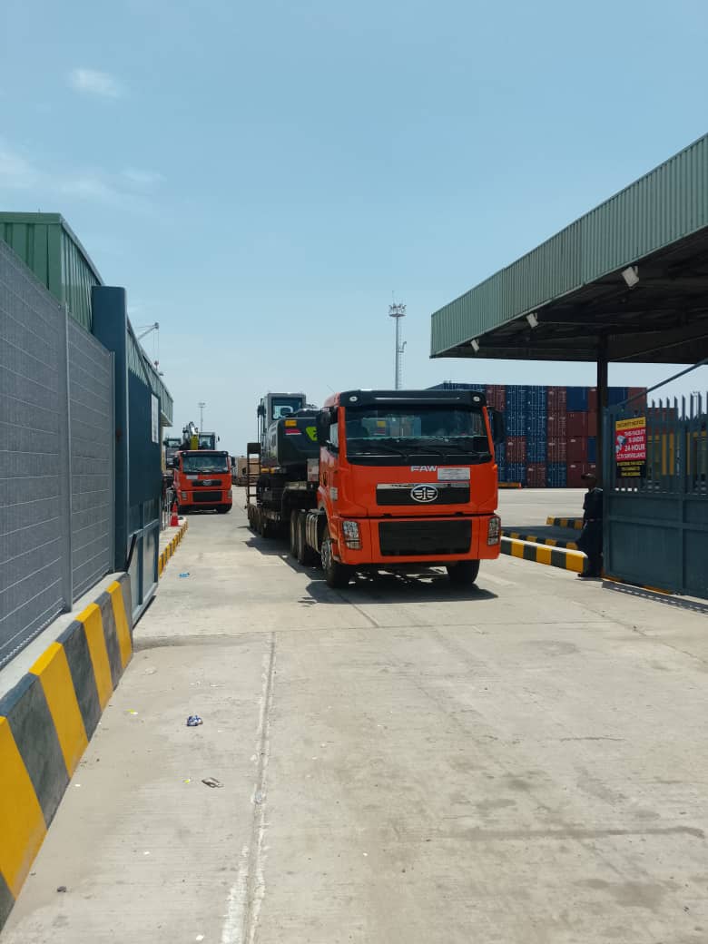 FAW truck carrying construction machinery at a logistics yard